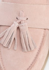 Rosa Wildleder-Lederschuhe mit flachem Design, dekorativen Quasten und kontrastierenden Nähten entlang der Kanten für zusätzliche Details.