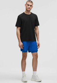 Svart t-shirt med korta ärmar i kombination med ljusblå shorts. Klädseln har en enkel design och t-shirten har en rund halsringning.