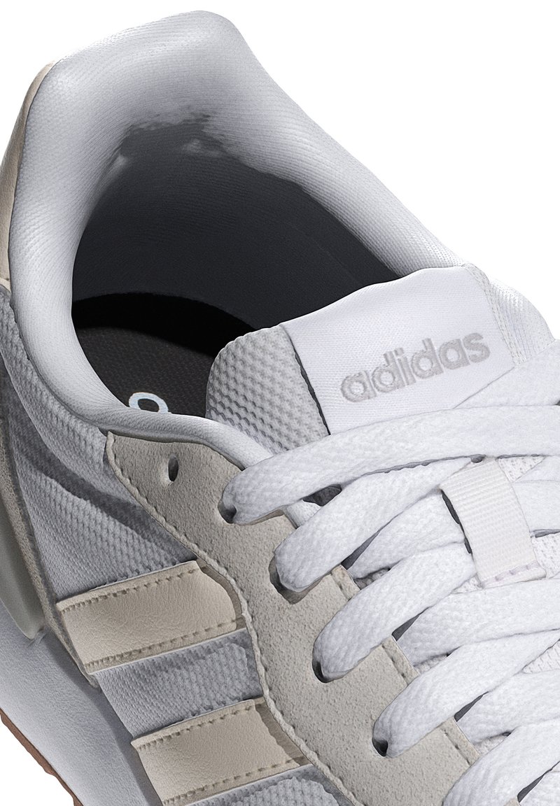 Zapatilla blanca con materiales de malla y cuero, detalles en gris, parte superior texturizada, cordones planos y un cuello acolchado con un logo en la lengüeta.