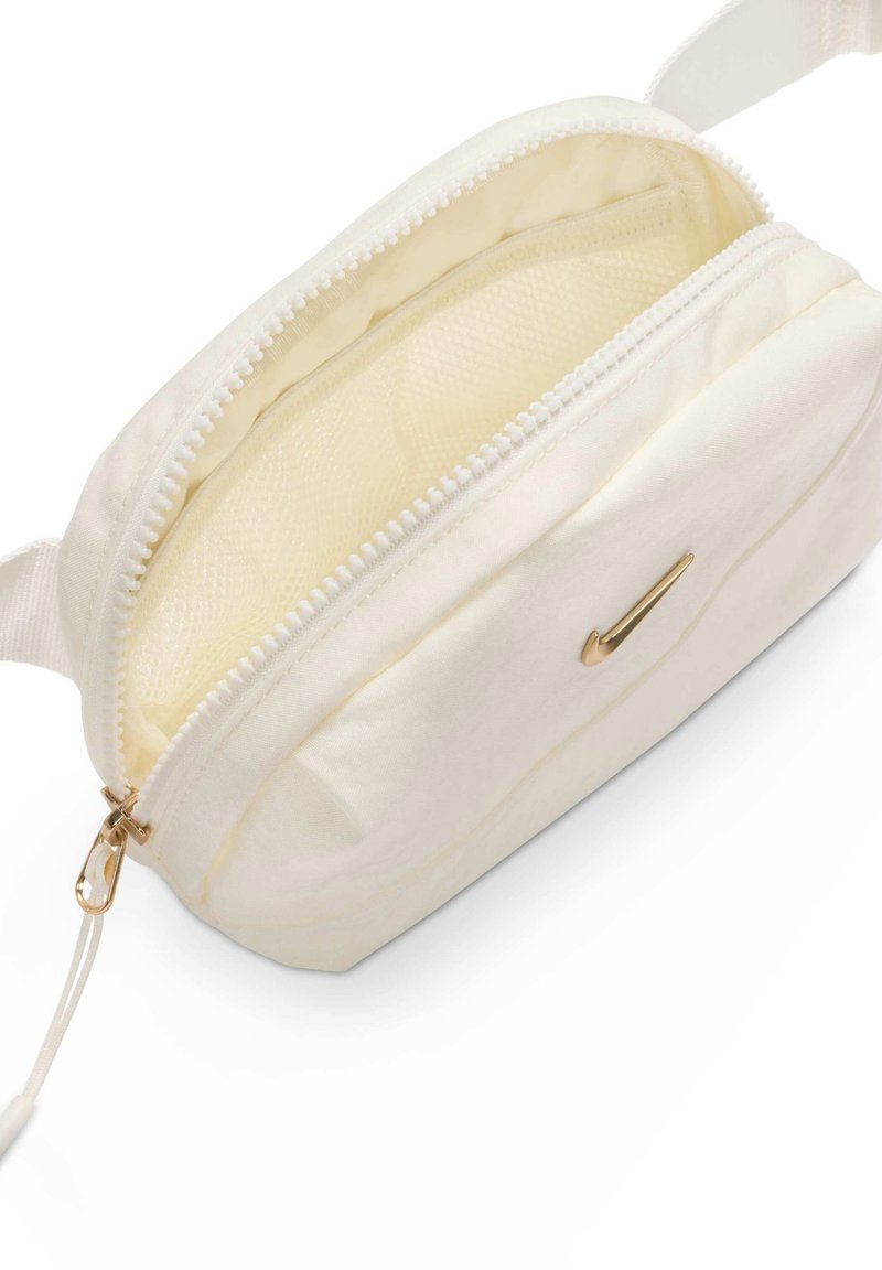 Bustina di tessuto color crema con cerniera dorata e piccolo swoosh Nike dorato sul davanti, mostrata parzialmente aperta con interno vuoto.