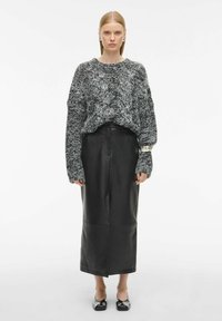Falda de cuero negra de longitud media combinada con un suéter de punto grueso gris de corte oversize. Textura suave, ajuste holgado, con mangas anchas y sin patrones visibles.