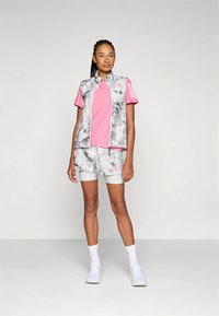 Súprava športového oblečenia obsahujúca sivú a bielu mramorovanú vestu, ružové tričko a nohavice s potlačou. Vyrobené z priedušnej tkaniny so športovými detailmi.