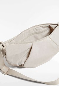 Beige szövet övtáska texturált külsővel. Cipzáras záródás, belső zsebbel rendelkezik. Állíthatópánt a sokoldalú viselet érdekében.