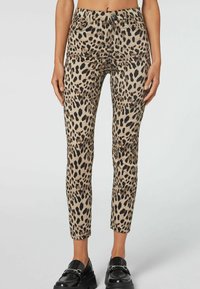 Jeans slim fit in tessuto beige e nero con stampa leopardata, dotati di tasche posteriori e zip sul davanti. Texture liscia con motivi distintivi.