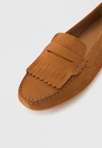 Καφέ σουέντ μοκασίνι με λεπτομέρεια φράντζας στην κορυφή, ραμμένα άκρα και λείο στρογγυλεμένο μυτερό άκρο.