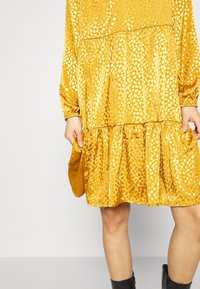 Gul, löst sittande klänning i mjukt tyg, med en tärningsdesign och textur av upphöjda prickar samt långa ärmar.