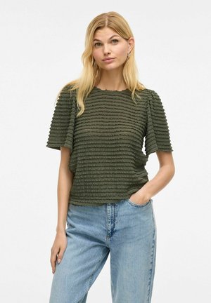 Blouse verte texturée avec des rayures horizontales ondulées ; manches courtes ; encolure ronde ; associée à un jean bleu clair.