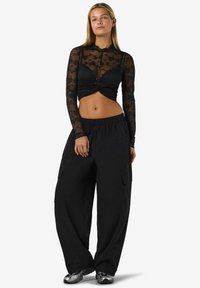 Fekete csipkeből készült, hosszú ujjú felső virágmintával, laza szabású fekete cargo nadrággal párosítva. A deréknál csomózott díszítéssel.