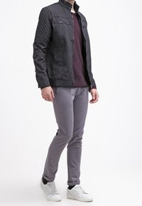 Černá prošívaná bunda s vysoce postaveným límcem, šedý texturovaný svetr, světle šedé slim-fit kalhoty a bílé tenisky. Bunda má zipové kapsy.