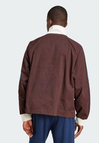 Casaco castanho cropped com um colarinho branco, apresentando detalhes azuis nas mangas e um corte descontraído. Feito de um tecido texturizado.