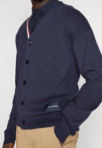 Marineblauer Knopf-Cardigan aus Strickstoff, mit V-Ausschnitt, gerippten Akzenten und einem Markenetikett am Saum.