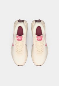 Αθλητικά παπούτσια Nike για τρέξιμο με επάνω μέρος από κρεμ διαπνέον υλικό, ροζ λεπτομέρειες, κλειστό σύστημα κορδονιών και μπορντό εσωτερική επένδυση. Στρογγυλωμένη μύτη και ελαφριά σόλα.