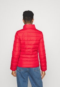 Rode pufferjack met een horizontaal gestikt patroon, hoge kraag en lange mouwen. Het materiaal lijkt glanzend en lichtgewicht.