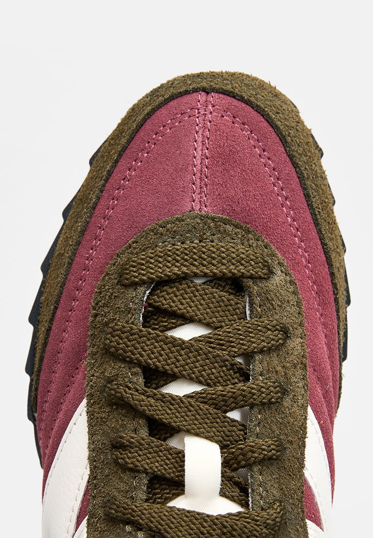 Zapatilla deportiva con parte superior de ante burdeos, acentos en verde oliva, cordones marrones y un diseño de raya blanca en el lateral. Suela de goma texturizada.