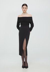 Czarny sweter z odkrytymi ramionami i prążkowanym wzorem, zestawiony z czarną spódnicą ołówiastą z wysokim rozcięciem, obie części wykonane z gładkiego materiału, uzupełnione czarnymi butami na obcasie.