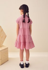 Vestito rosso e bianco a quadretti vichy con maniche corte e balze arricciate. Indossato con scarpe nere e calzini bianchi, acconciatura con due trecce.