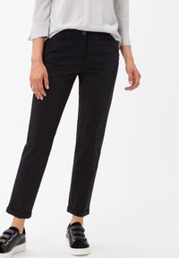 Černé bavlněné kalhoty s rovnými nohavicemi, předními kapsami a zapínáním na jeden knoflík, doplněné o černé tenisky.