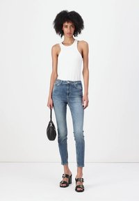 Top bianco a costine, jeans skinny in denim blu, sandali neri con tacco a blocco e fibbie, e una piccola borsa nera.