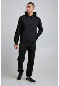 Melnā kapuci ar priekšējo kabatu, auklām un ribu aprocēm, apvienota ar tumšiem sašaurinātiem treniņbikšu un melnām sporta apavām. Gluda tekstūra.