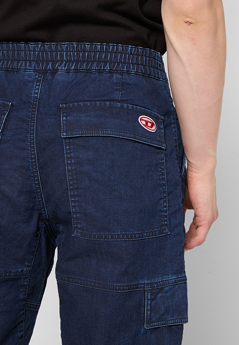 Donkerblauwe cargo-broeken van denim met een elastische tailleband en meerdere zakken. Heeft een rood logo-opdruk op de achterzak.