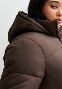 Brązowa kurtka puchowa z kapturem, z quiltowanym wzorem, gładką teksturą materiału i pełnym zamkiem błyskawicznym z przodu.