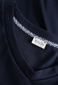 Tummansininen paita, jossa on V-pääntie ja sinivalkoinen kuvioitu koriste. Siinä on "RÖSCH"-merkki. Sileä, pehmeä kangas.