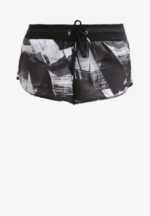 Femme marchant vêtue d'un débardeur sportif noir avec des rayures orange, d'un short noir à motifs et de baskets blanches avec des rayures argentées.