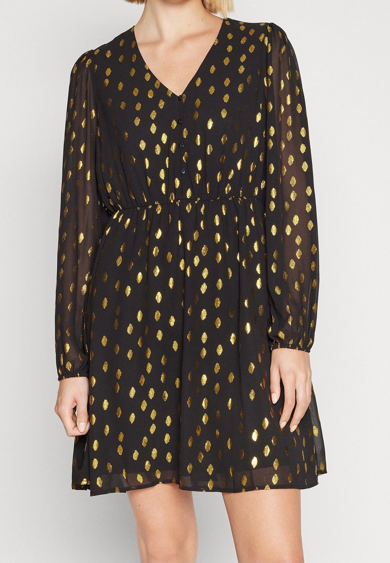 Robe noire à manches longues avec motif ovale métallique doré, col en V, boutons à l'avant, taille cintrée et manches en tissu transparent.