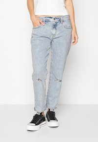 Vaaleansiniset farkut väljällä leikkauksella, joissa on kuluneet repeämät polvissa ja käännetytlahkeet. Yhdistetty mustiin matalavartisiin tennareihin.