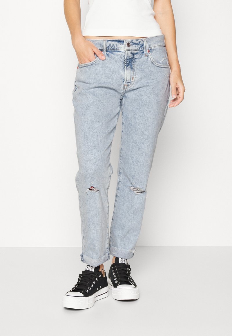 Vaaleansiniset farkut väljällä leikkauksella, joissa on kuluneet repeämät polvissa ja käännetytlahkeet. Yhdistetty mustiin matalavartisiin tennareihin.