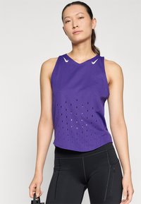 Top de sport sans manches violet avec un col en V, présentant des trous découpés pour la ventilation et des accents de logo blancs sur les épaules.