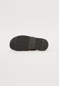 Semelle de chaussure en caoutchouc noir avec un motif de semelle en zigzag. Présente un profil plat et sans marque visible. Adaptée pour la traction et la stabilité.