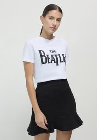 T-shirt bianco in cotone con la scritta "THE BEATLES" in grassetto nero, abbinato a una minigonna nera a campana.