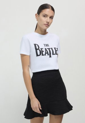 Weißes Baumwoll-T-Shirt mit dem Text "THE BEATLES" in fetter schwarzer Schrift, kombiniert mit einem schwarzen, ausgestellten Minirock.