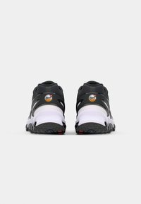 Zwart-witte sport schoenen met een bovenwerk van mesh, rubberen zool en opvallende hielbranding met een oranje en zwart logo.