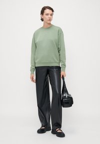 Lys grønn sweatshirt med hjerteformede detaljer, sammen med høyt liv svarte faux skinnbukser. Modellen holder en svart håndveske.