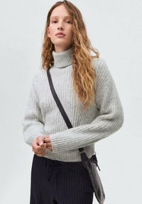 Maglione a collo alto grigio chiaro a coste con maniche lunghe, caratterizzato da una vestibilità rilassata. Abbinato a pantaloni scuri e una borsa nera a tracolla.