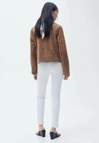 Rjava semiš kratka jakna, oprijete bele jeans hlače, črne masivne pete in beli šal zvezan zadaj, prikazano s hrbtne strani.