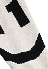 Nærbilde av hvit strikket stoff med det store svarte tallet "1" og en del av en buet svart form, sannsynligvis en detalj fra en sokk eller erme.