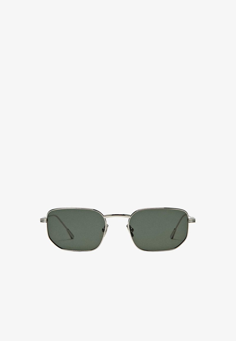 Lunettes de soleil rectangulaires avec des verres vert foncé. Monture en métal argenté fin avec une finition polie et branches élancées. Design minimaliste.