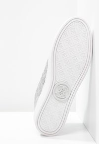 Šedá textilní teniska s bílou gumovou podrážkou, která má texturovaný vzor a kruhový logo detail na patě.