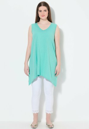 Túnica sin mangas de color verde menta con escote en V y dobladillo asimétrico, combinada con pantalones capri blancos que presentan un borde de encaje en el dobladillo.