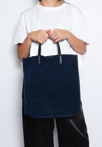 Navy blauwe suède schoudertas met zwarte leren handvatten. Rechthoekige vorm, minimalistisch ontwerp, gladde textuur en geen zichtbare patronen of accenten.