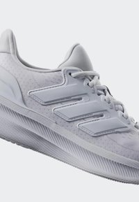 Witte sportieve schoen met een gestructureerde mesh bovenkant, een drie-strepenontwerp in dezelfde kleur en een rubberen zool met een patroon.