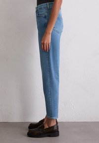 Jasnoniebieskie dżinsy z tapered fit, pięcioma kieszeniami i przeszyciami. Noszone z ciemnobrązowymi mokasynami.