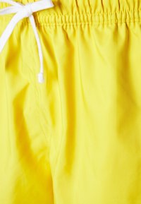 Lyse gule badeshorts med elastisk taljebånd og hvid snøre bundet i sløjfe.