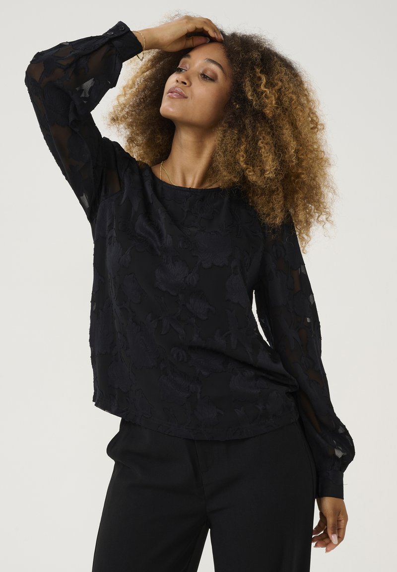 Blusa nera a fiori con texture, maniche lunghe e trasparenti, e polsini aderenti. Il tessuto ha una leggera lucentezza e intricate fantasie floreali.