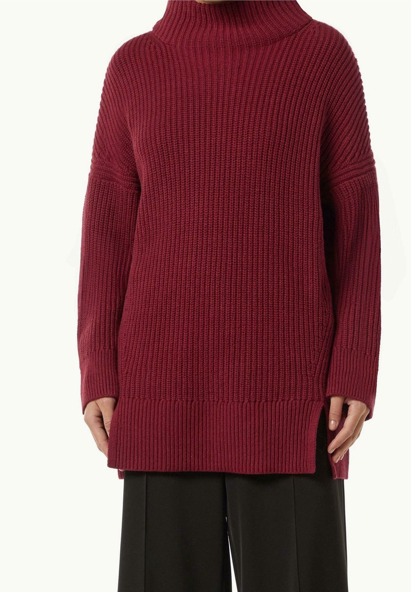 Pull à col roulé en maille côtelée bordeaux surdimensionné avec manches longues et fentes latérales, porté avec un pantalon noir à jambes larges.
