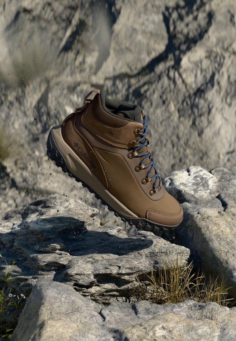 Brown hiking boot with a textured synthetic upper, padded collar, blue laces, and rugged outsole, set against rocky terrain.
