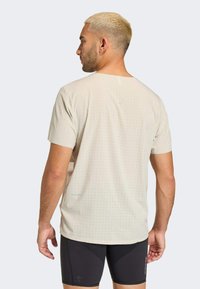 Μπεζ αθλητικό μπλουζάκι με τελεία σχέδιο, κοντά μανίκια και άνετη εφαρμογή. Το μοντέλο φοράει μαύρες σορτς, δακρύζοντας από πίσω.